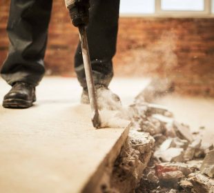 Construction worker using a jackhammer to break concrete floor with dust and debris flying