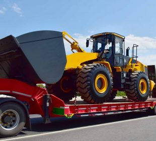 Yellow wheel loader secured on a red flatbed trailer for heavy equipment transport on a highway.