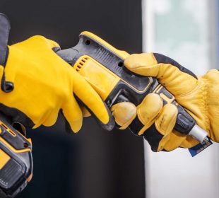 Two workers wearing yellow gloves exchanging a cordless power drill on site.