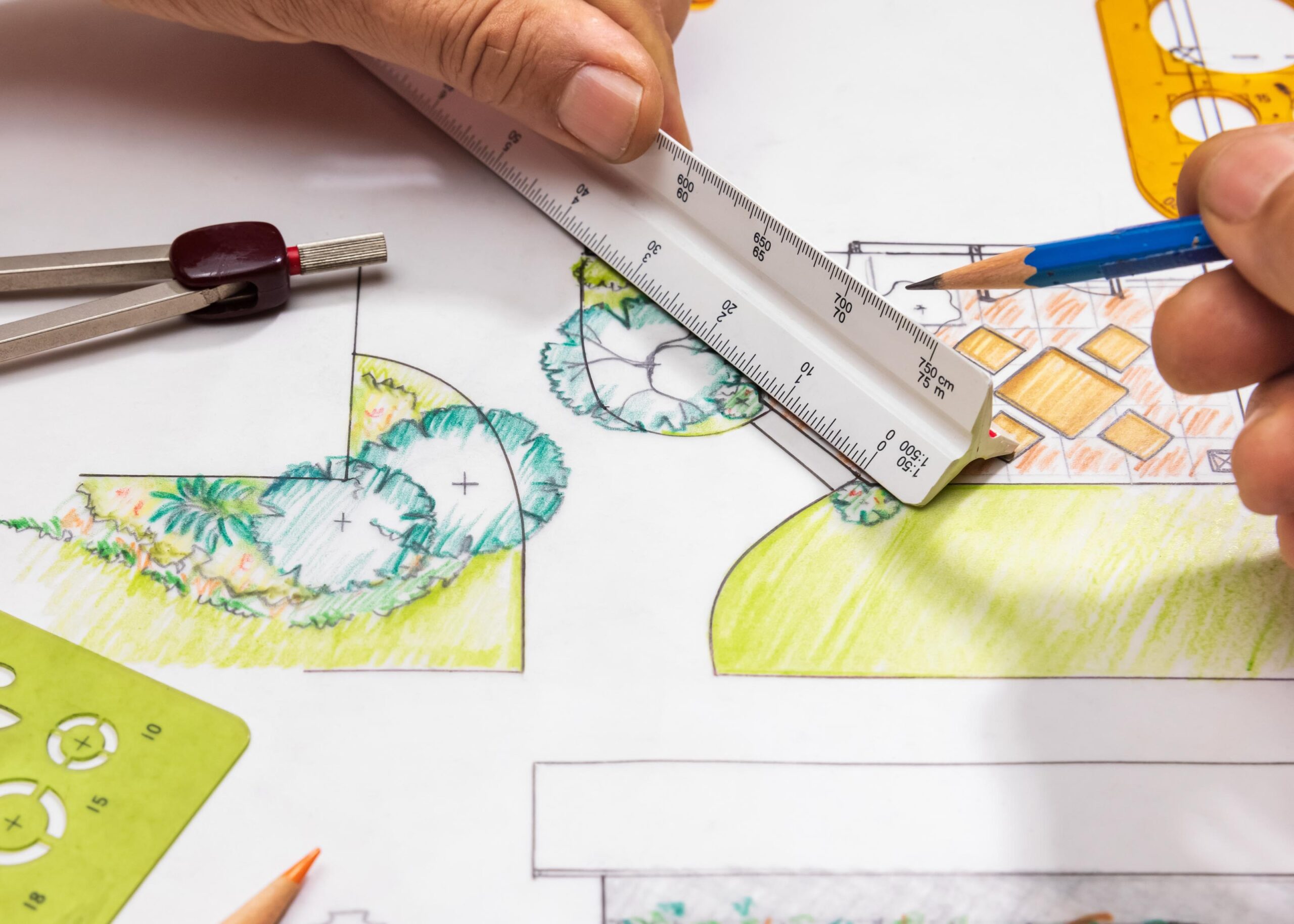 hands working on a landscape design plan using a ruler and pencil