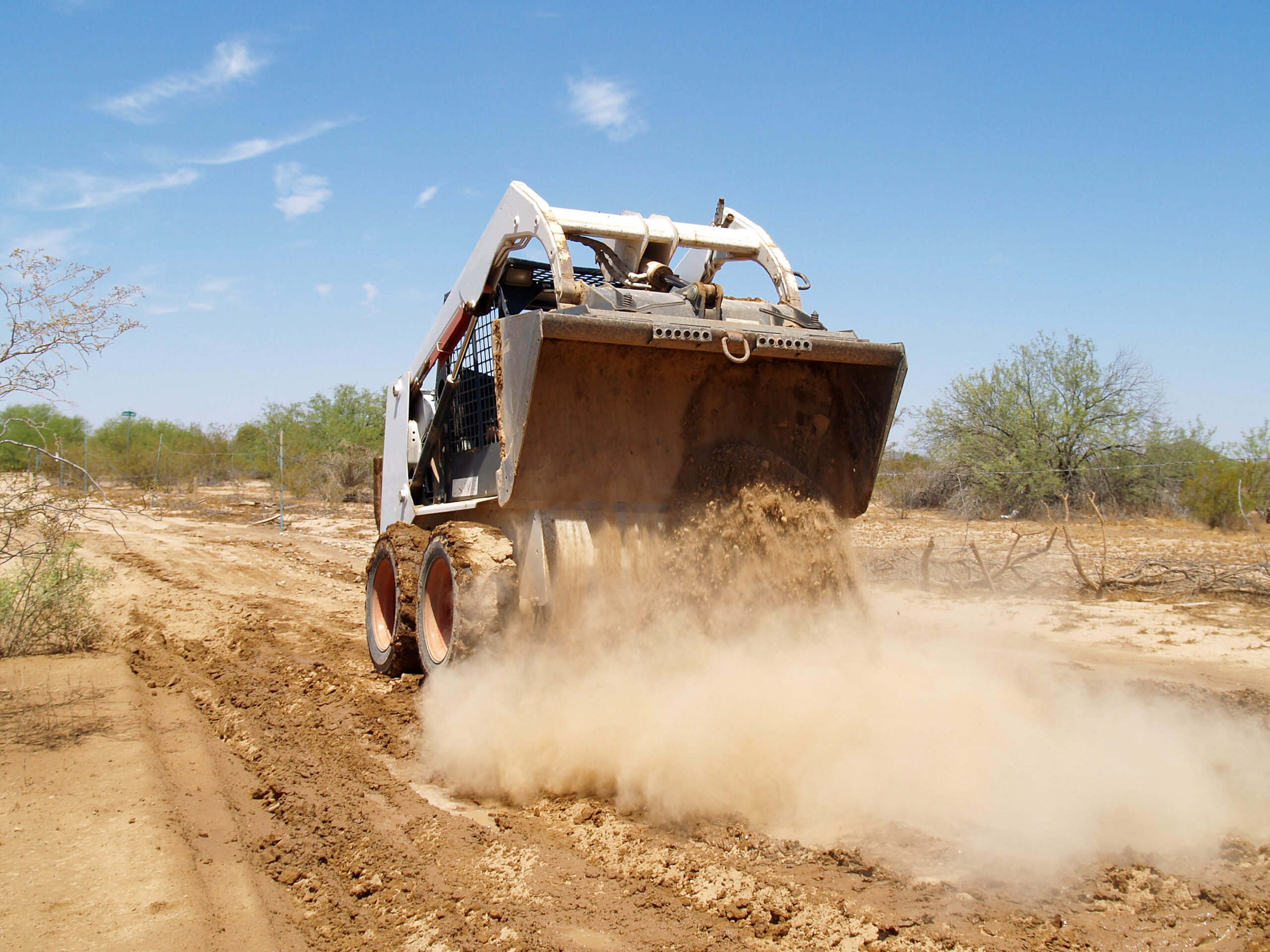 skid steer loader from trs equipment rental dumping dry soil dirt on a road