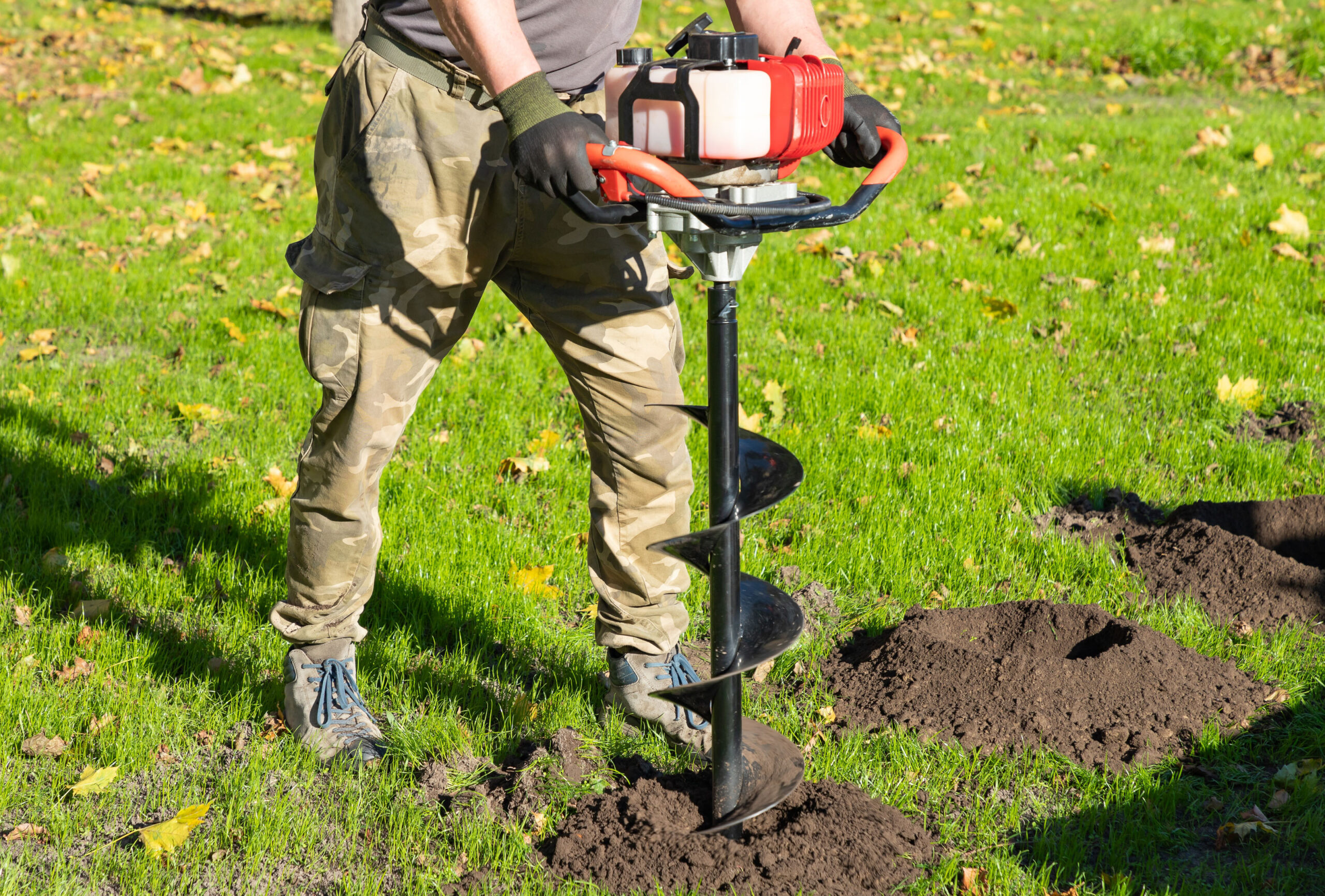 a man drilling hole in grassy yard with a gas powered auger from trs equipment rental