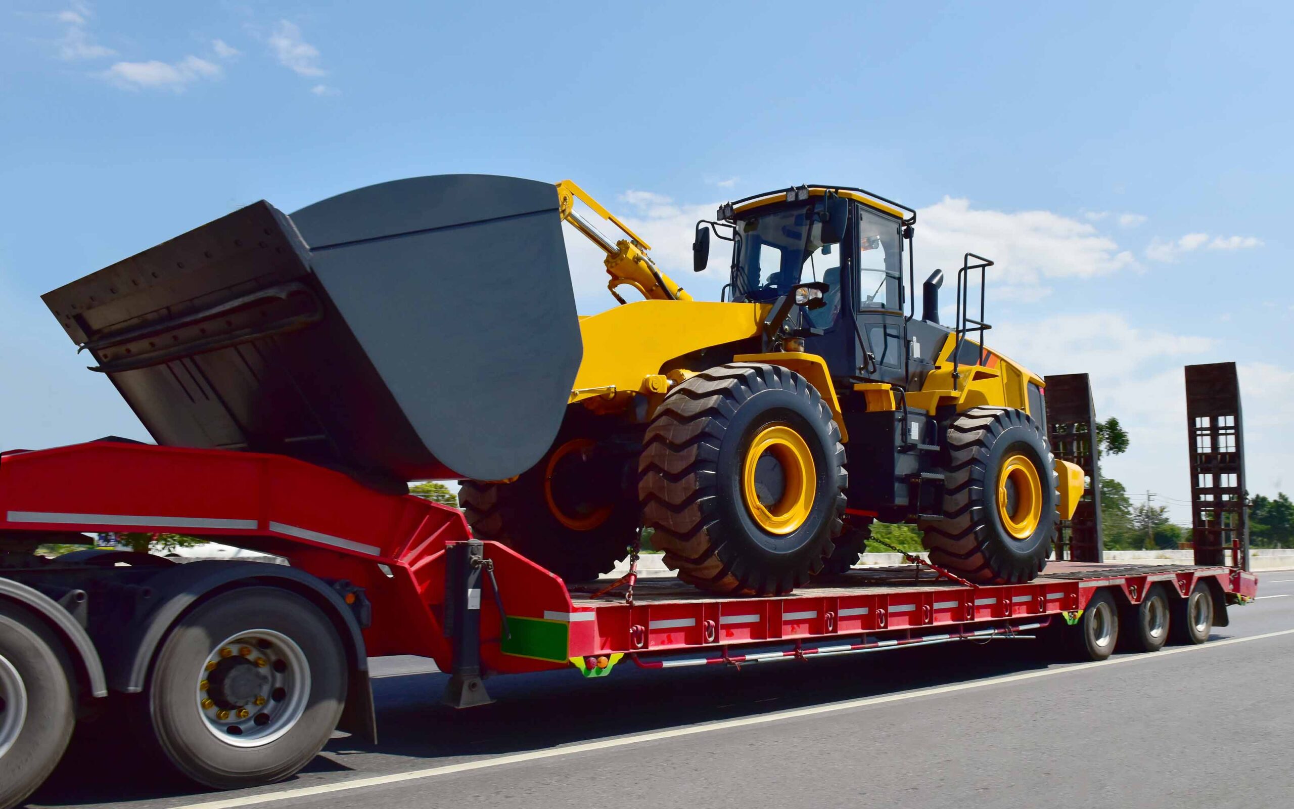 Yellow wheel loader secured on a red flatbed trailer for heavy equipment transport on a highway.