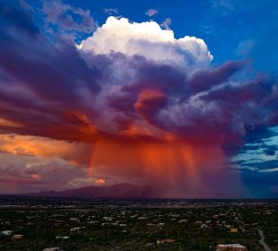 A dramatic sunset thunderstorm with vibrant colors of orange, red, and purple clouds over a landscape with scattered houses